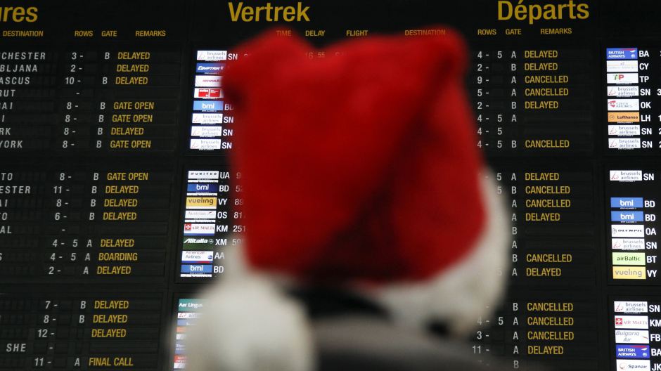 A passenger wearing a Santa Claus hat, looks at a departure board displaying cancelled and delayed flights at Zaventem international airport